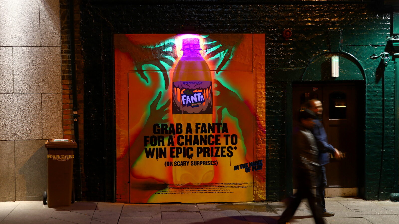 Street scene with Fanta Halloween billboard promoting prizes and surprises, featuring a bottle of Fanta Orange and bold seasonal messaging